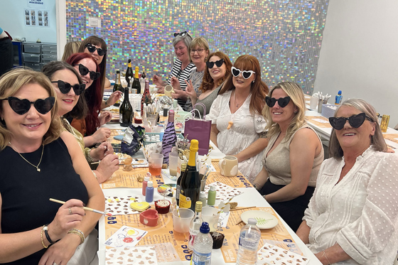 Hen party wearing love heart shaped sunglasses smile while pottery painting